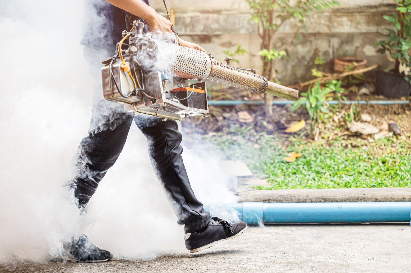 A person wearing a black shirt and pants uses a smoke machine for mosquito control in Honolulu, HI.
