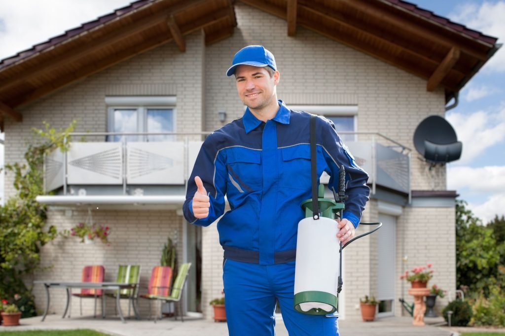 A man in blue overalls holds a sprayer and gives a thumbs up, symbolizing pest control services in Honolulu, HI.